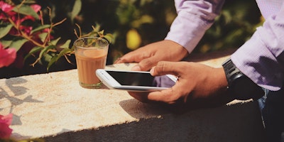 A man uses a mobile phone while enjoying a coffee.