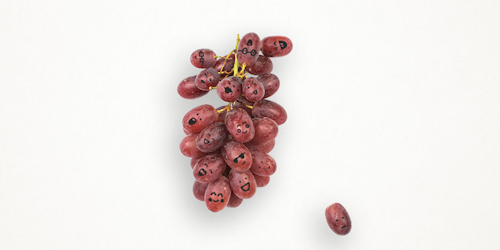 A bunch of red grapes with little faces drawn on in black ink.