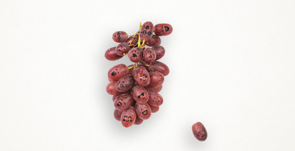 A bunch of red grapes with little faces drawn on in black ink.