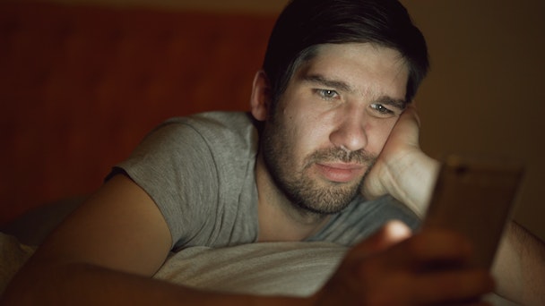 A man lies in bed looking at social media posts.