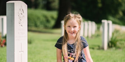 A little girl kneeling beside a war grave.