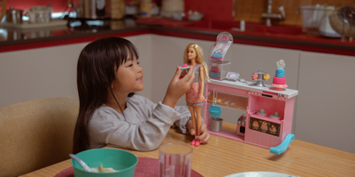 Little girl plays with Barbie at dinner table
