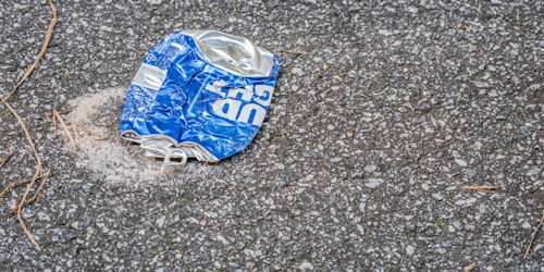 Crushed Bud Light beer can flattened on black asphalt