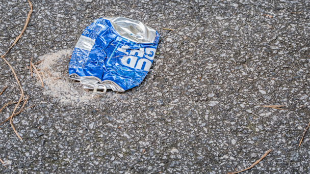 Crushed Bud Light beer can flattened on black asphalt