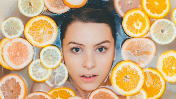 Woman's face in bathwater surrounded by orange slices