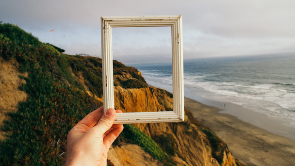 Person holding frame over seaside background