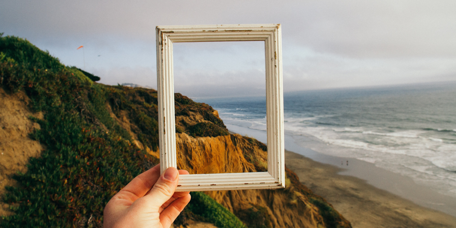 Person holding frame over seaside background