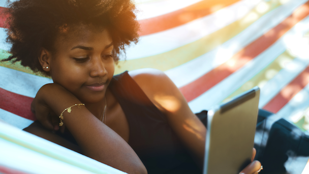 Black woman laying in hammock reading from a tablet