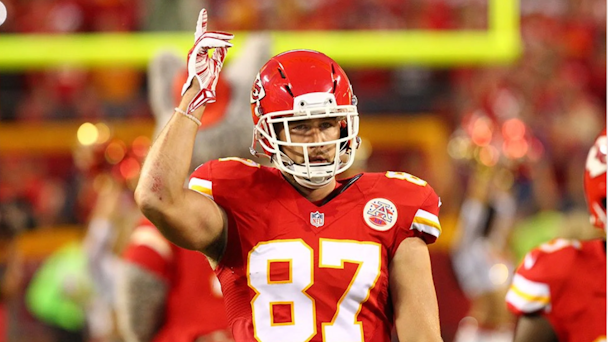 Travis Kelce in Kansas City Chiefs red uniform raising a finger to the sky