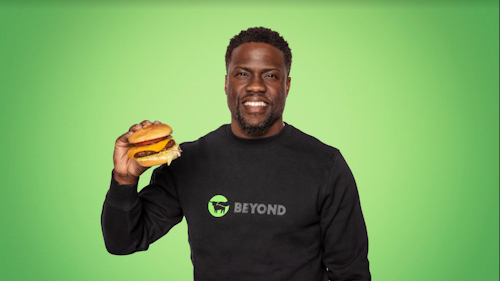 Kevin Hart holding a Beyond Meat burger against a green backdrop
