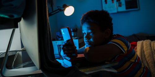 Kid using computer and phone in dark room
