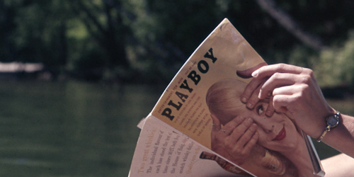 Hands holding old Playboy magazine with lake in background