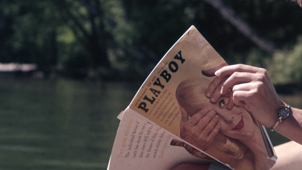 Hands holding old Playboy magazine with lake in background