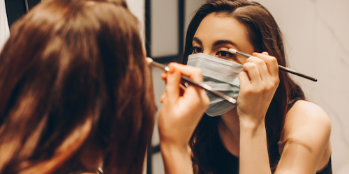 Woman applying makeup while wearing face mask