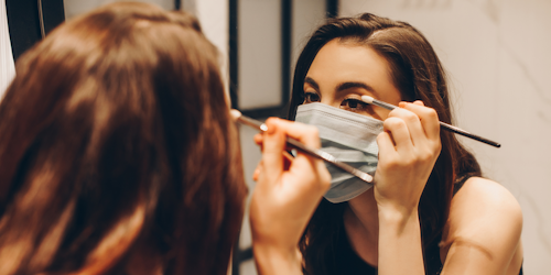 Woman applying makeup while wearing face mask