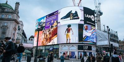 Digital billboards in bustling square with people walking around