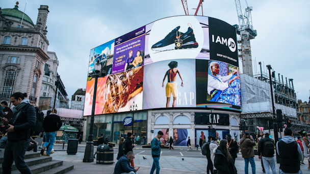 Digital billboards in bustling square with people walking around