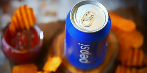 Can of Pepsi soda among orange chips and dip on table