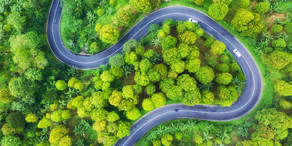 Aerial view of curving road through forest with two cars on the road