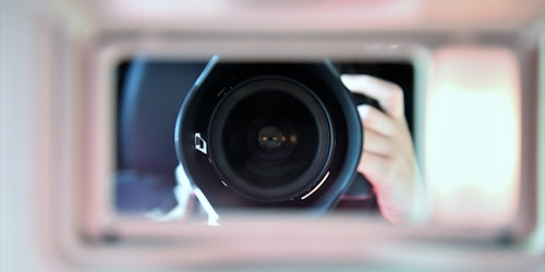 A camera lens looking through a window, reflected in a mirror