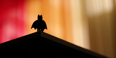 A lego figurine of Batman, in shadow on a ccolorful background