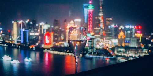 A flute of sparkling drink in front of the skyline of Shanghai, China