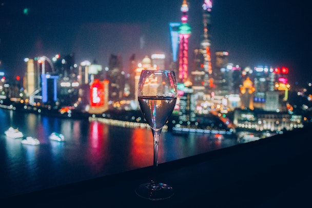 A flute of sparkling drink in front of the skyline of Shanghai, China