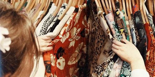 A shopper parting a rail of clothing, like a curtain