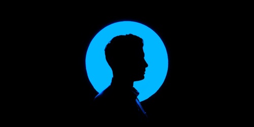 A person's head, in silhouette and profile, against a blue circular light