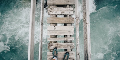 A pair of feet, stepping onto a rickety wooden bridge