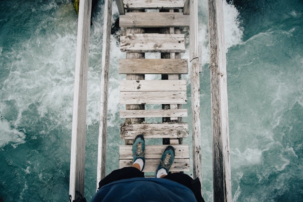 A pair of feet, stepping onto a rickety wooden bridge