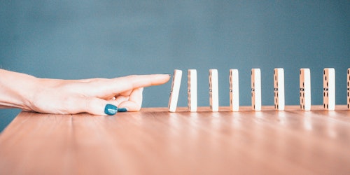 A finger, knocking over a row of dominos