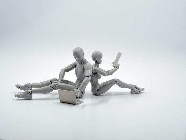 Two back-to-back grey mannequins, playing with grey tech