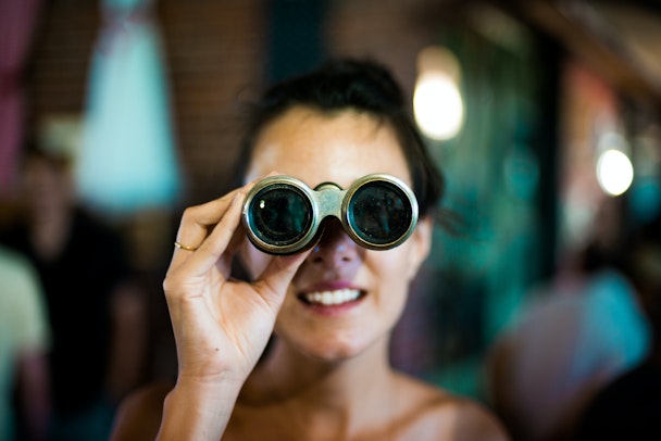 A person peering through a pair of brass binoculars