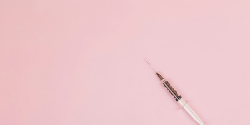 A syringe against a pink background