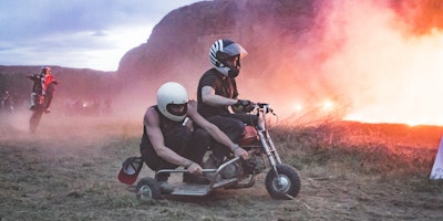 Two men on a makeshift motorcycle-and-sidecar, riding around a fire