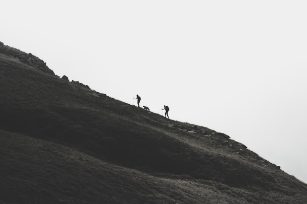 Two people and a dog, in silhouette climbing a hill