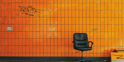 A desk chair on a street, in front of an orange wall