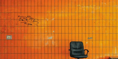A desk chair on a street, in front of an orange wall