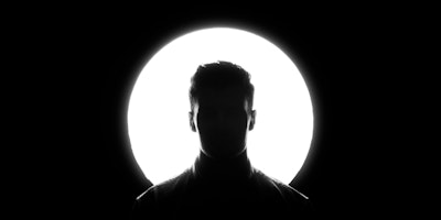 A person's head in silhouette against a round spotlight