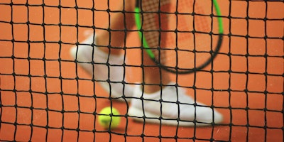A tennis player and ball behind a tennis net