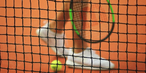 A tennis player and ball behind a tennis net