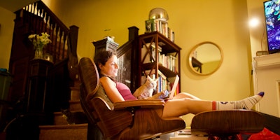 A person reclining on a comfortable chair with a laptop and a cat on their lap