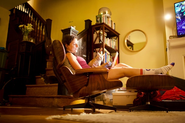 A person reclining on a comfortable chair with a laptop and a cat on their lap