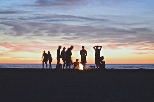 A group of young people, in silhouette, at a beach at sunset