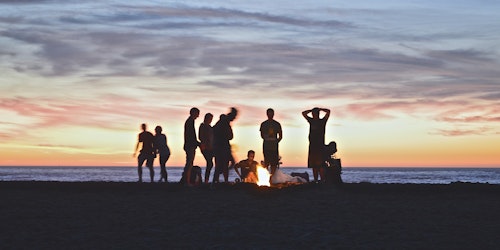 A group of young people, in silhouette, at a beach at sunset