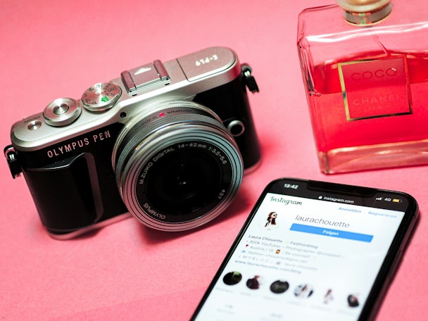 A camera, a perfume bottle, and a smartphone on a pink background