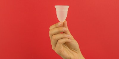 A moon cup, being help up against a red background