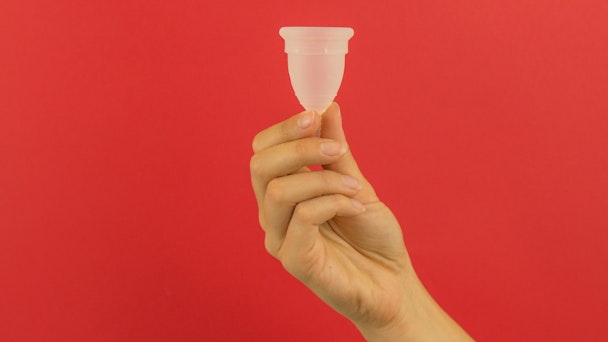 A moon cup, being help up against a red background