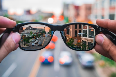 A pair of glasses, held up and reflecting a city street